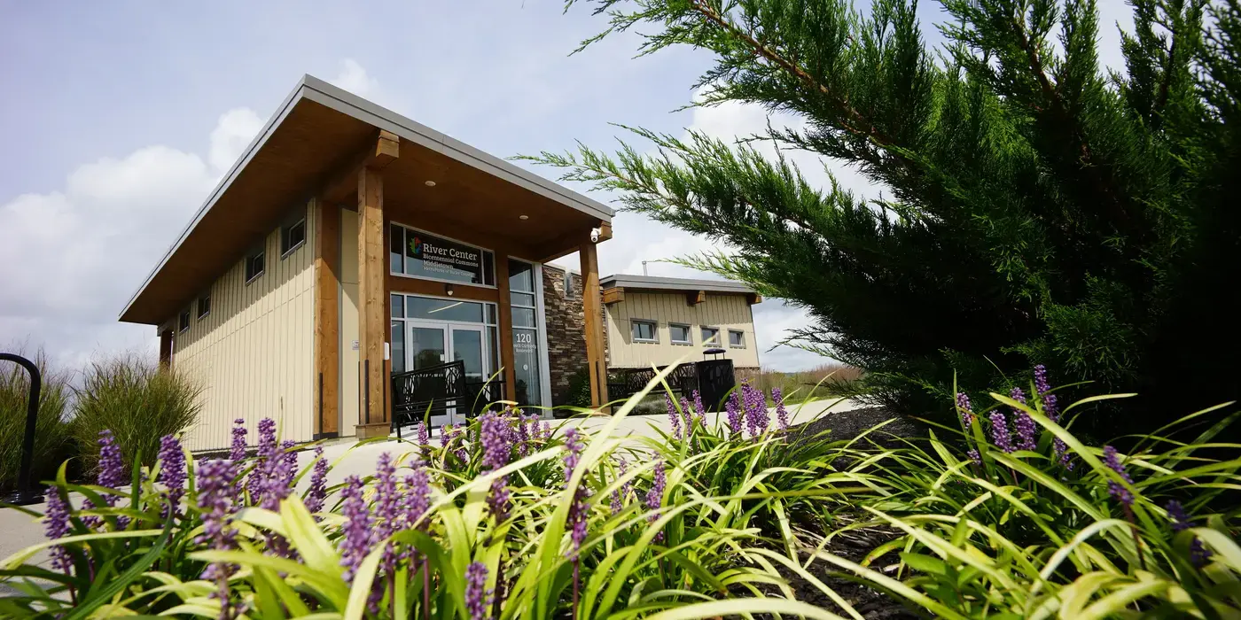 Middletown River Center - Middletown, OH Modern building with a sloped roof, foreground of purple flowers and green shrubs.