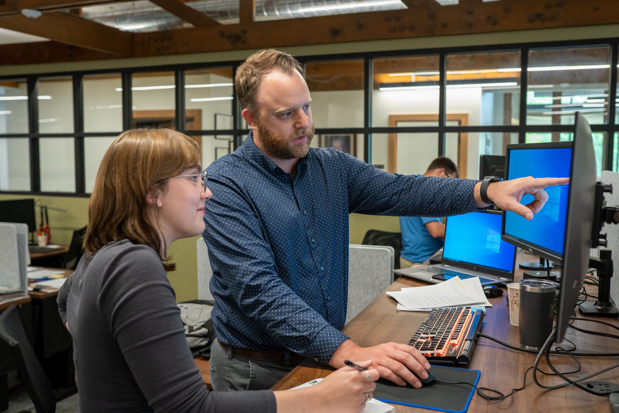 Bayer Becker Careers Two colleagues discuss work at a computer in a modern office.
