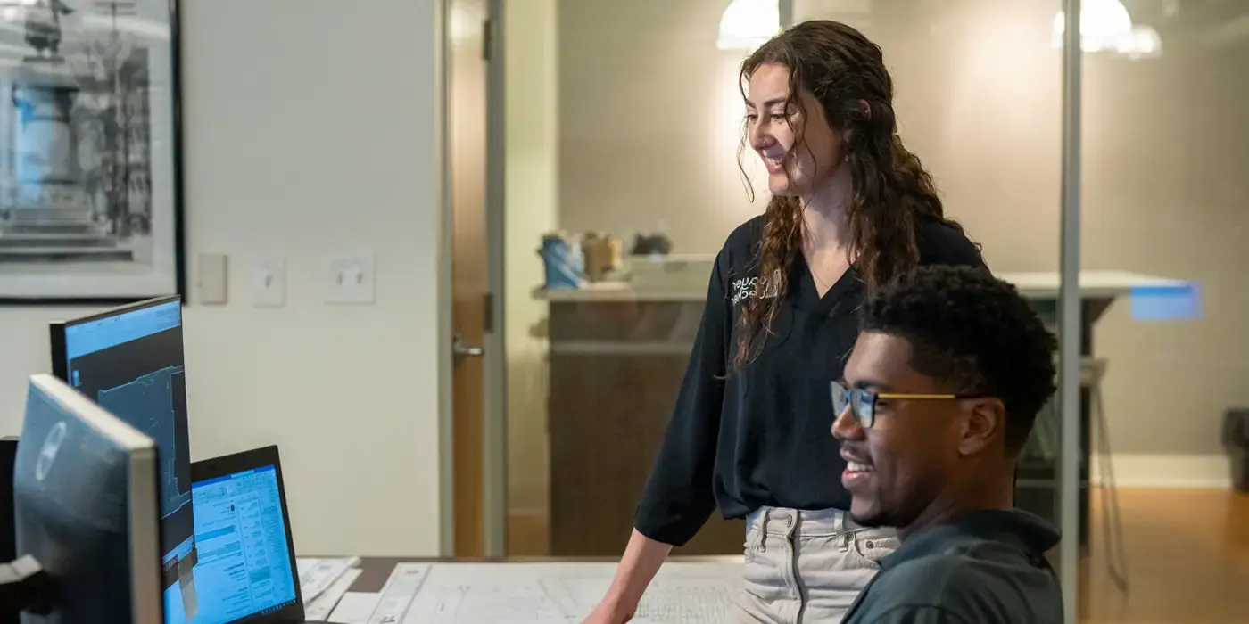 Two colleagues smiling while working at computers in an office.