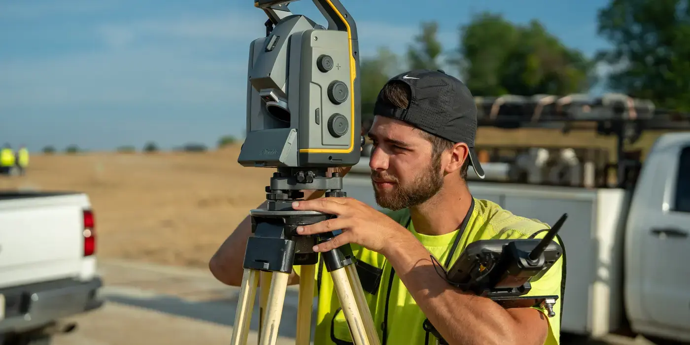 Bayer Becker Careers Surveyor using a theodolite on a sunny construction site.